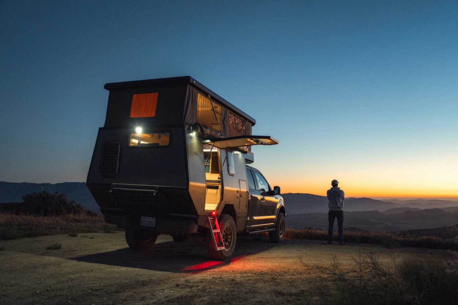 A camper truck parked at a ridgeline at dusk, last light over the valley